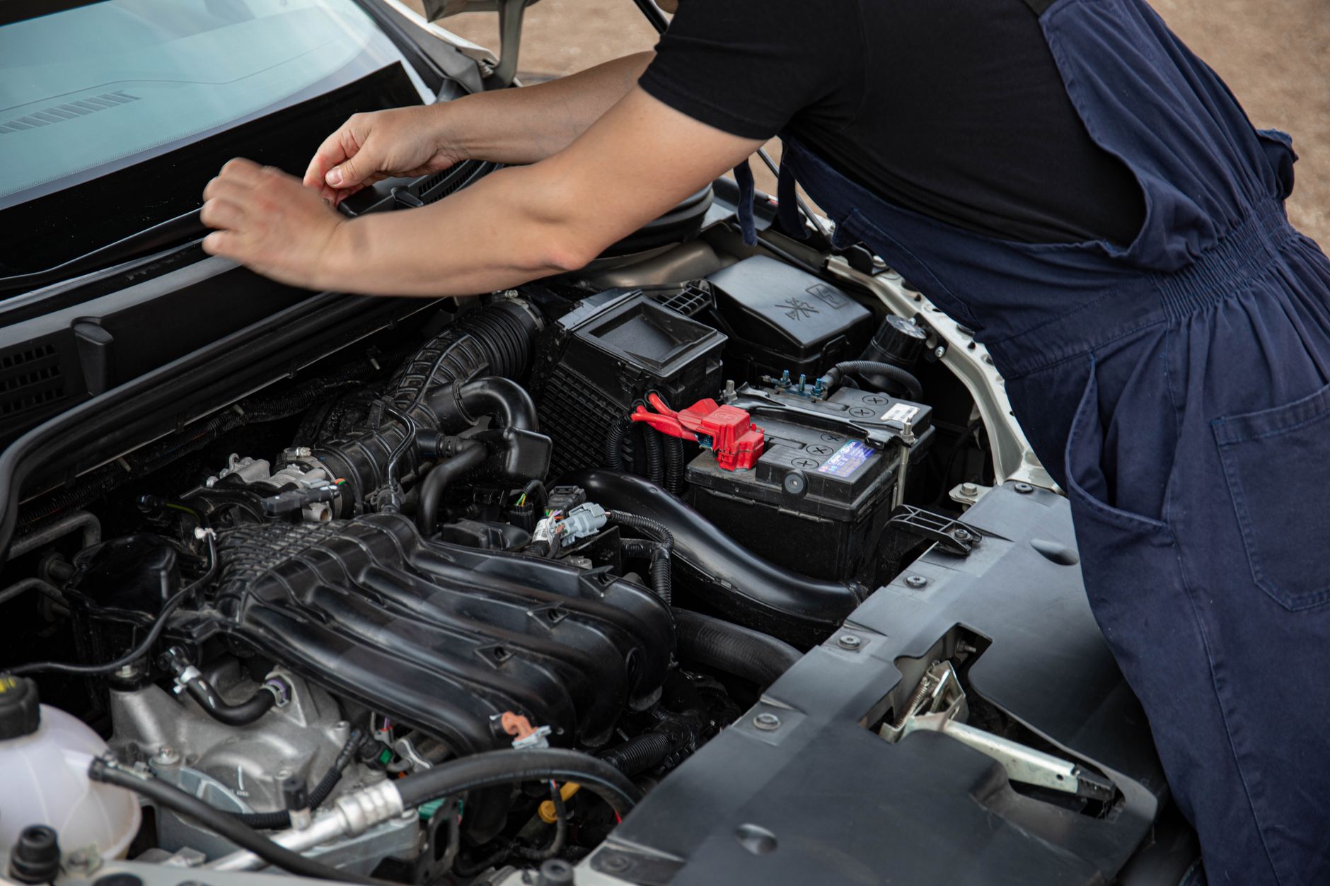 Mechanic performing maintenance on a car engine outdoors during the day. — Learn About Signs Your House Needs a Fresh Paint